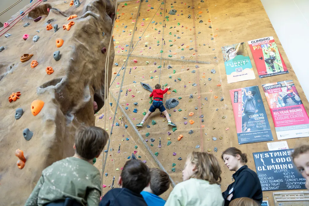 A child on a climbing wall while others watch at a FizzBug holiday club