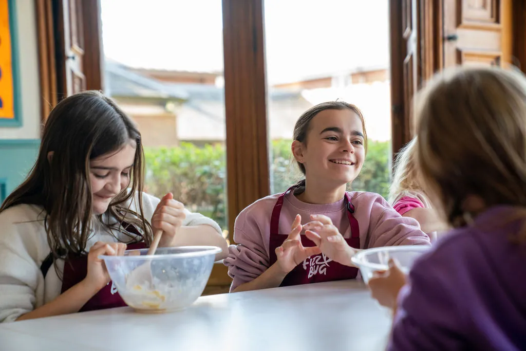 Children mixing ingredients in FizzBug aprons at a cookery session