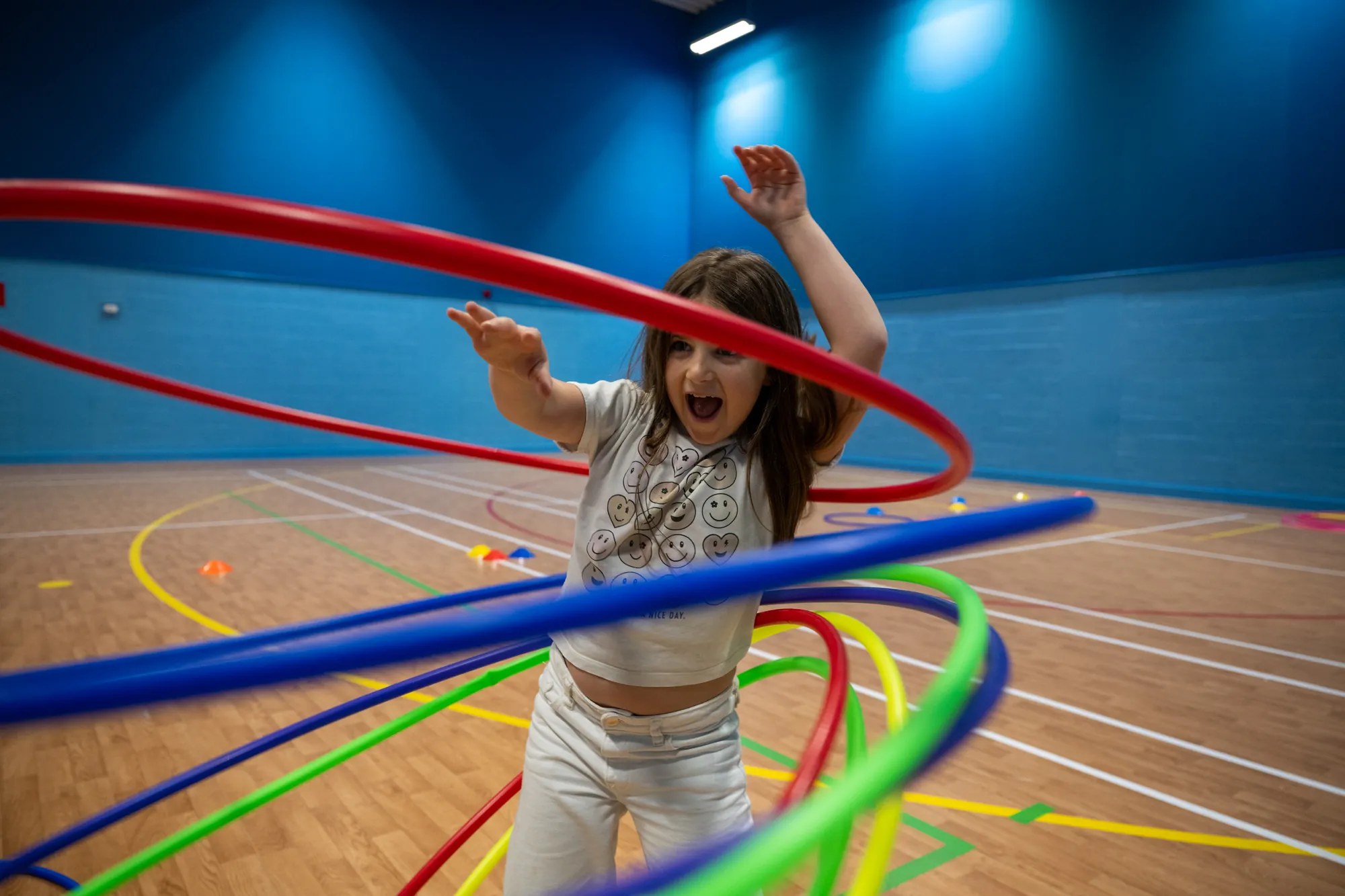 A girl playing with hula hoops in a sports hall at a FizzBug holiday club