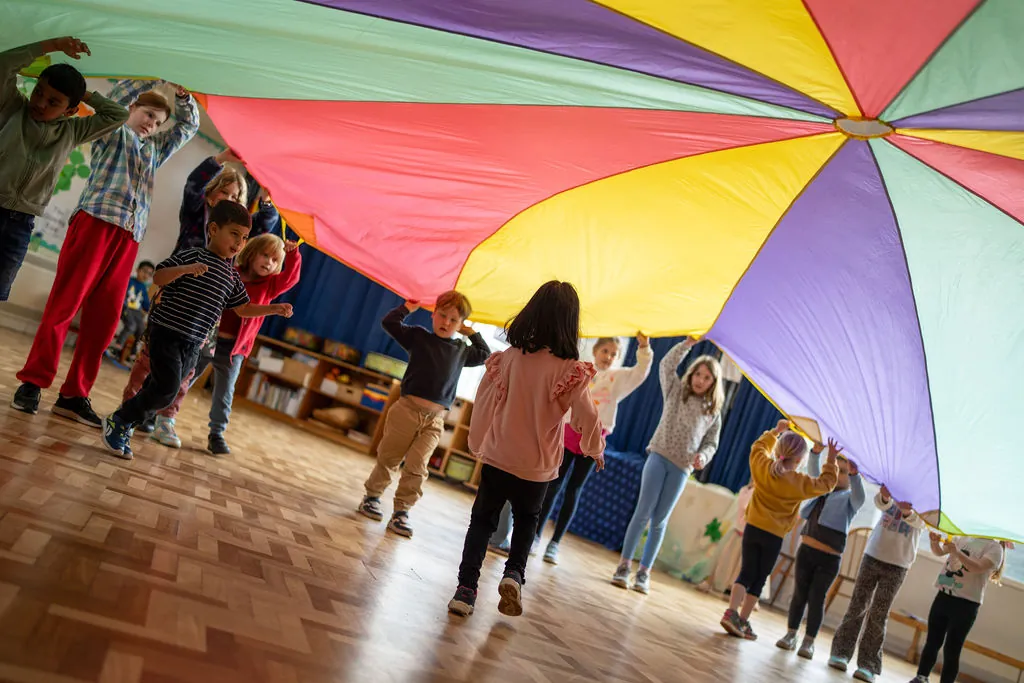 Children playing parachute games in a school hall at a FizzBug holiday club