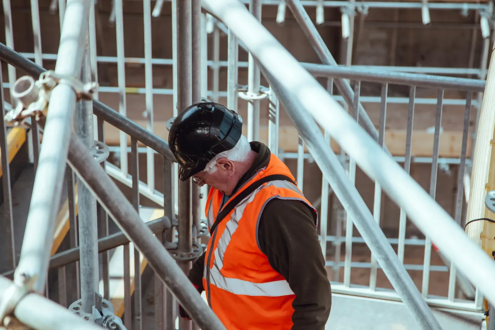 A site manager in a hard hat and hi-vis vest on scaffolding