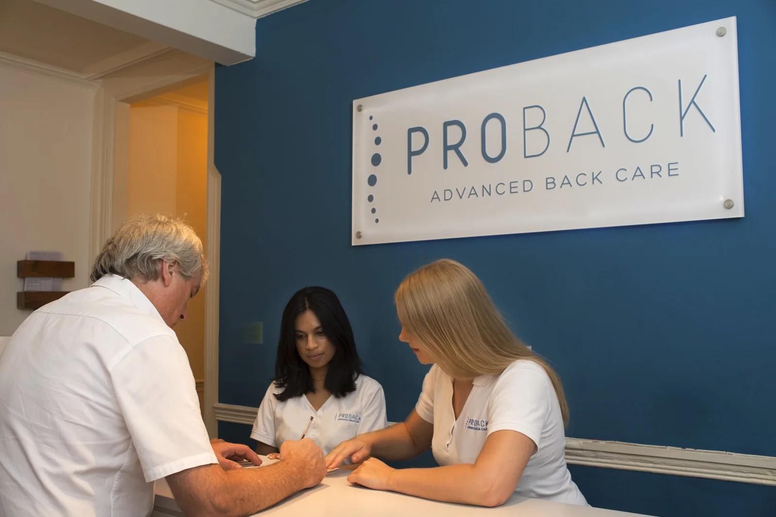 Clinicians at the Proback Victoria reception desk, beneath the Proback sign
