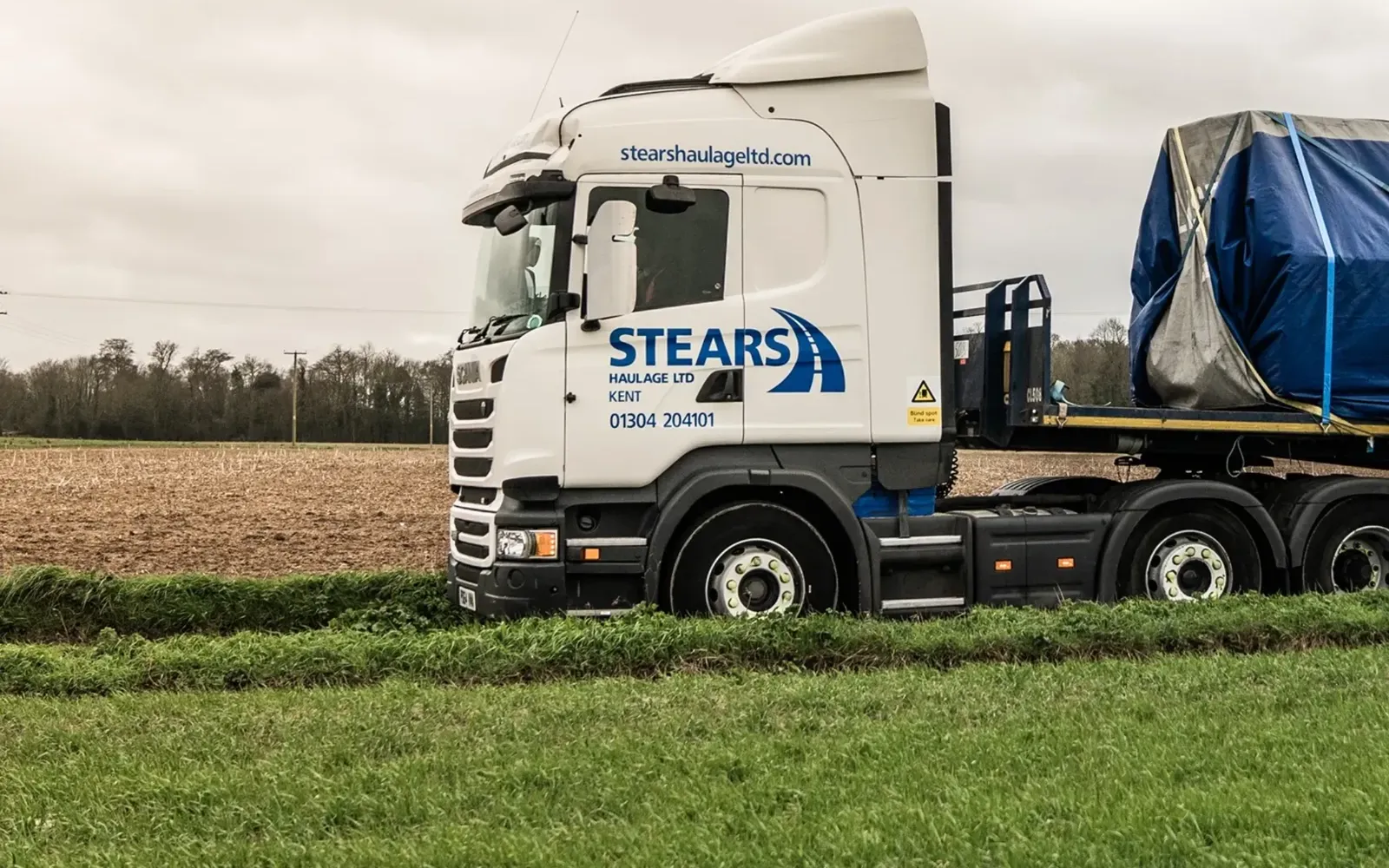 A Stears Haulage lorry with a sheeted load parked by a field